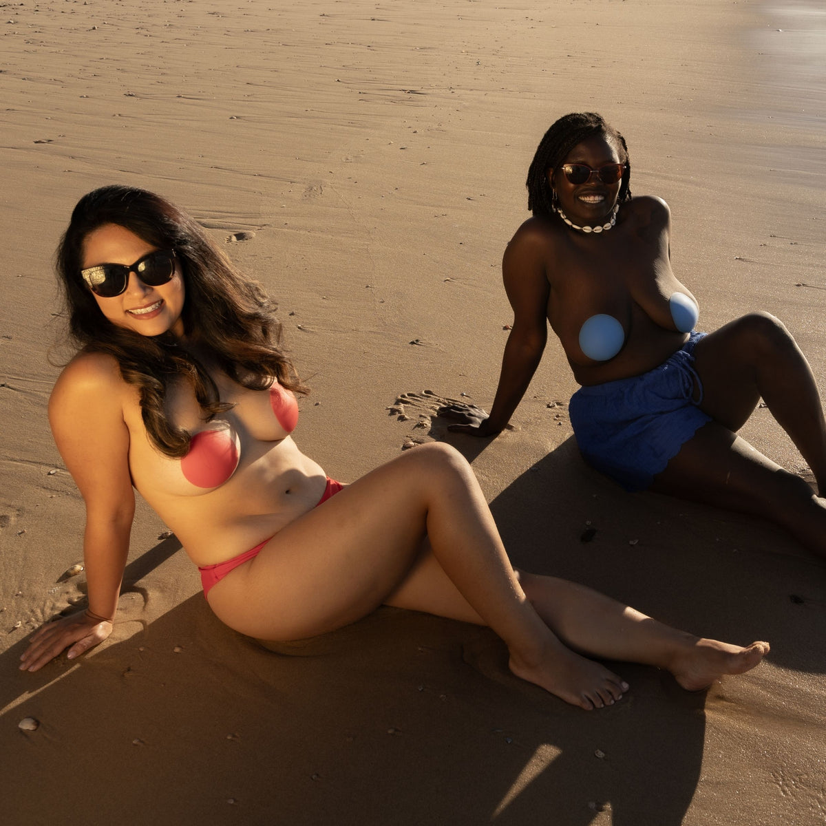 Two women on a sandy beach, wearing Noosa red and Bondi blue minuikini covers.